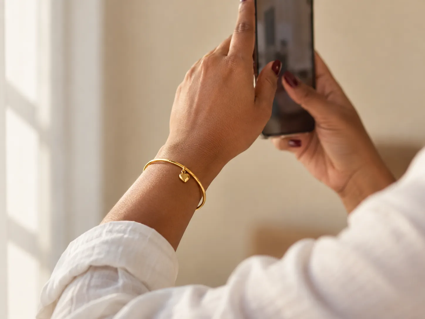 Filming a gold bangle with a heart charm on a phone to share