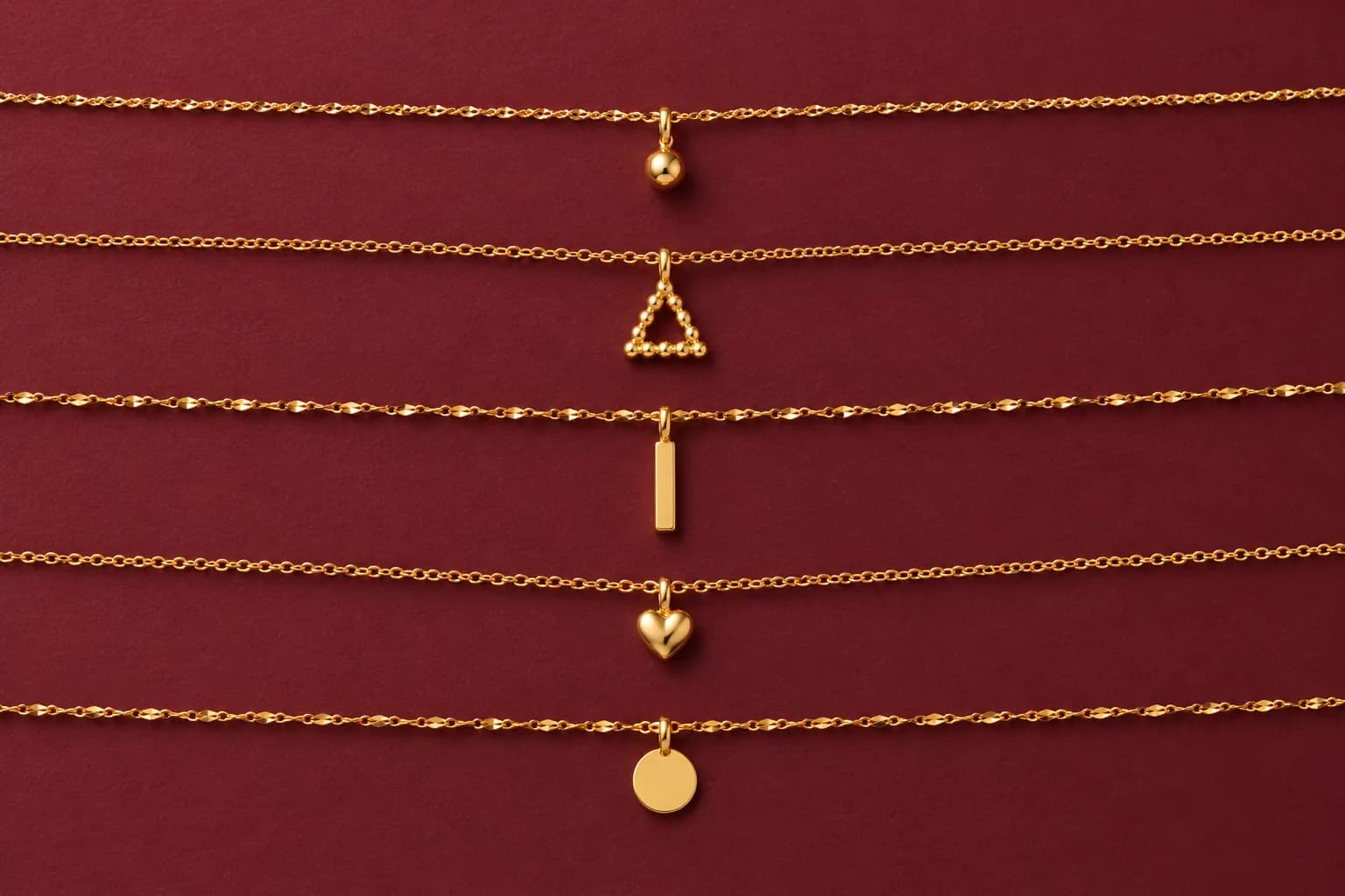 916 gold chains with small pendants laid out on burgundy