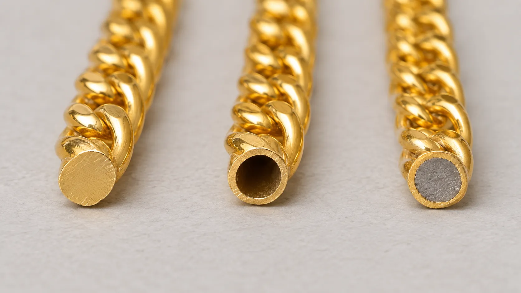 The cut ends of three gold chains: solid gold, a hollow gold tube, and a thin gold layer over grey base metal