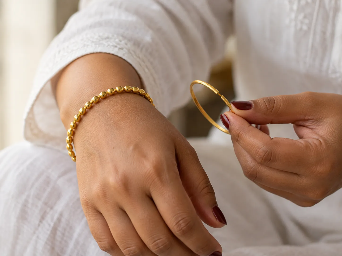 A woman wearing a new beaded gold bangle, holding an old gold bangle with a break in it