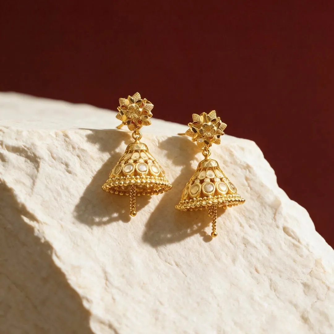 Gold jhumka earrings resting on white stone