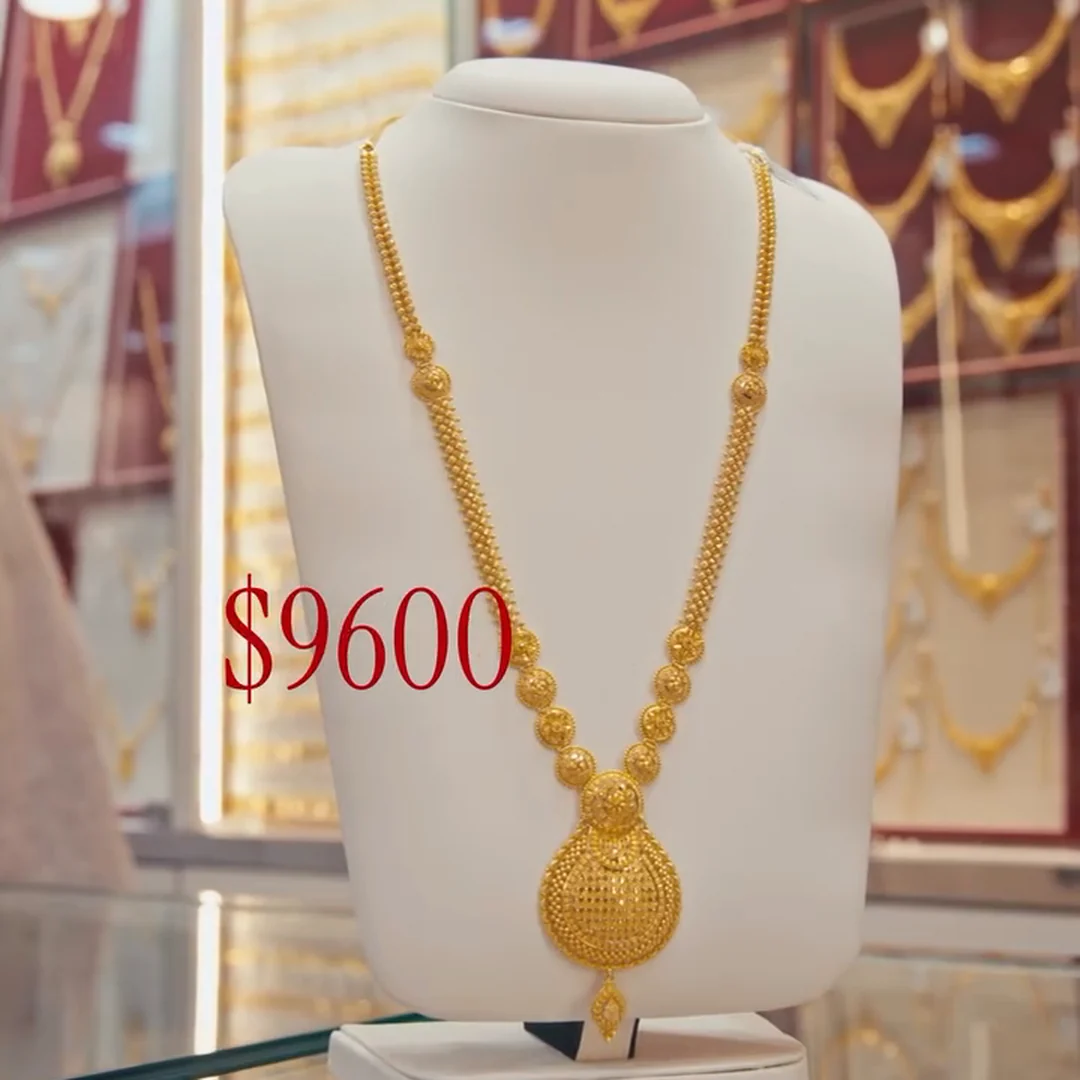 A long gold necklace with a filigree drop pendant on a display bust at the counter