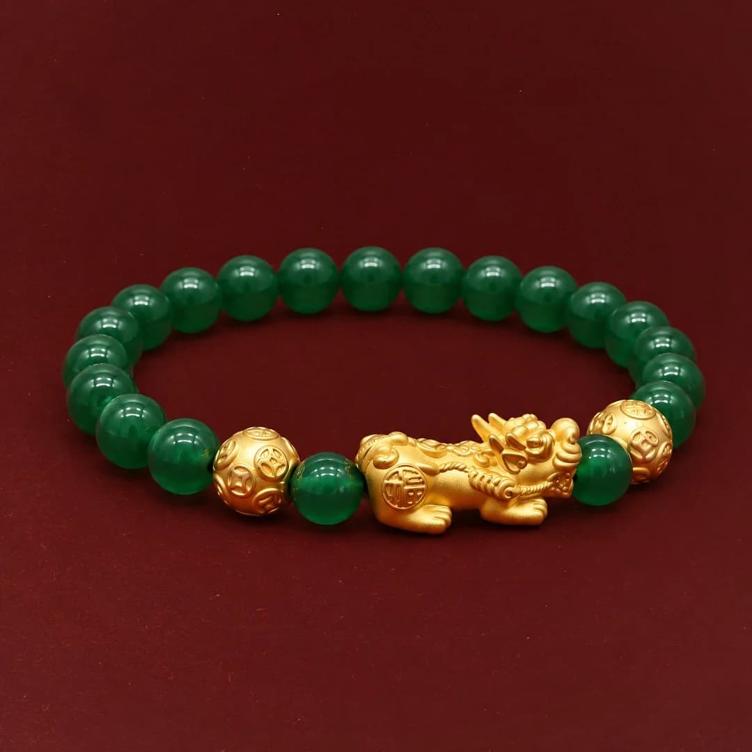 A Pixiu 916 gold bracelet with green beads and two gold coin beads, on burgundy