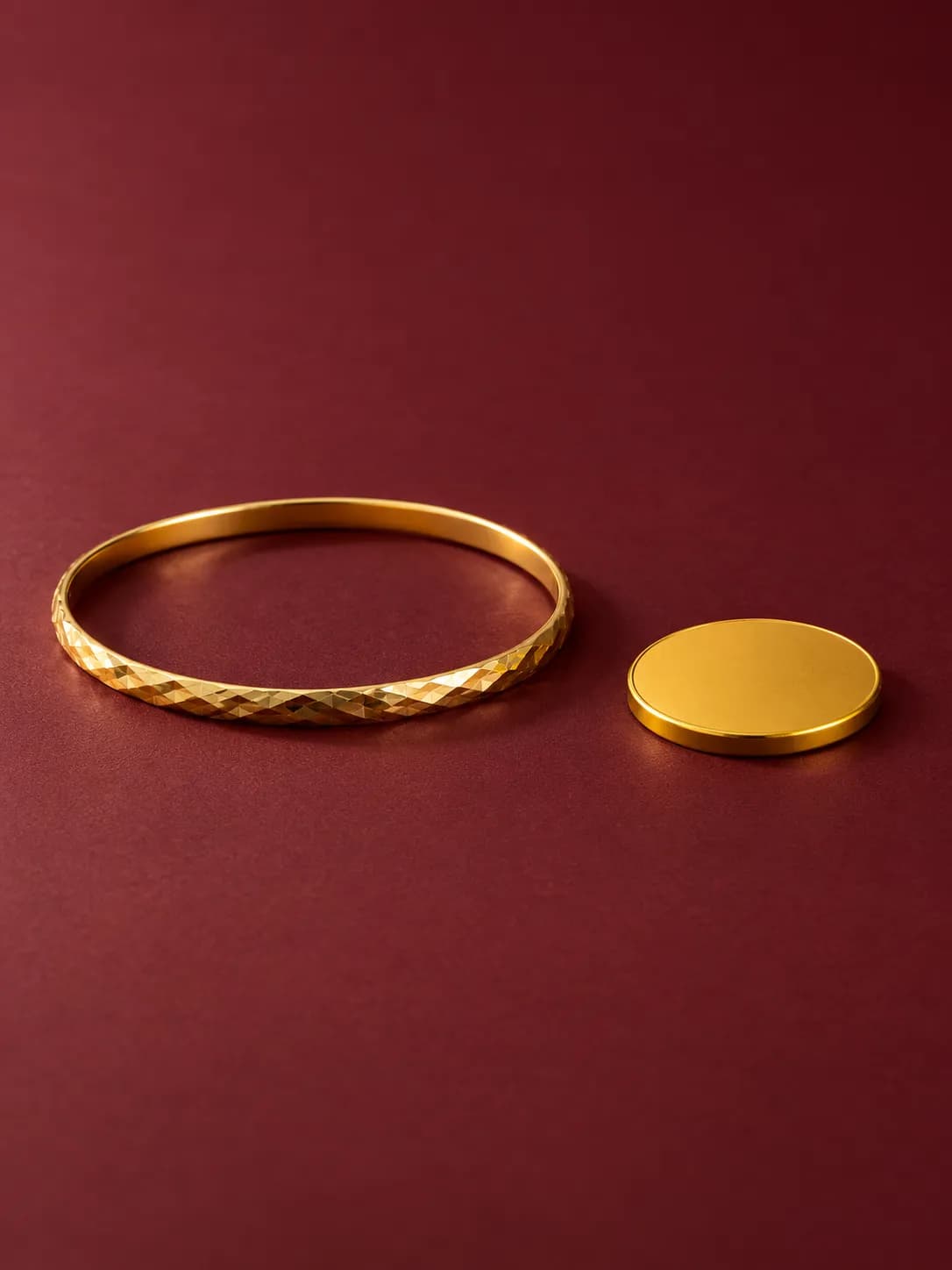 A 22K gold bangle beside a plain 24K gold coin on burgundy